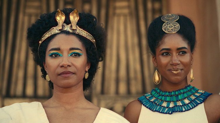 Cleopatra stands next to an older woman.