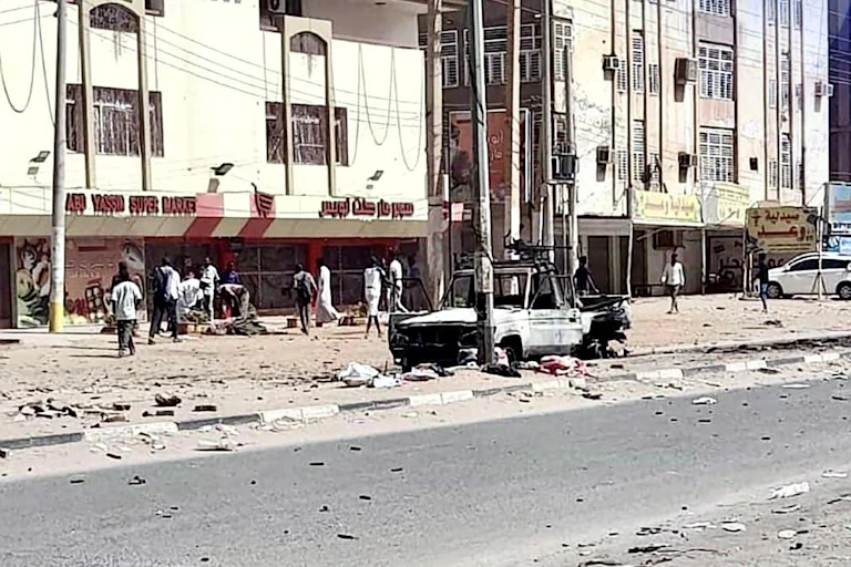 A street in Khartoum, Sudan, with a damaged truck in the foreground.