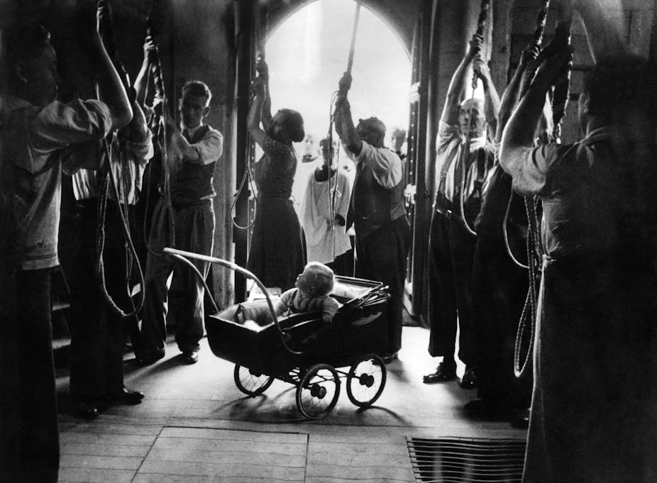 A baby in a buggy looks up at adults pulling on bell ropes.