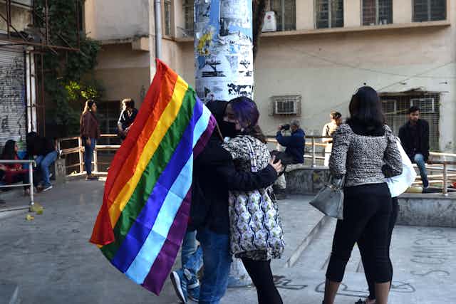 Students wearing masks and carrying the rainbow flag embrace 