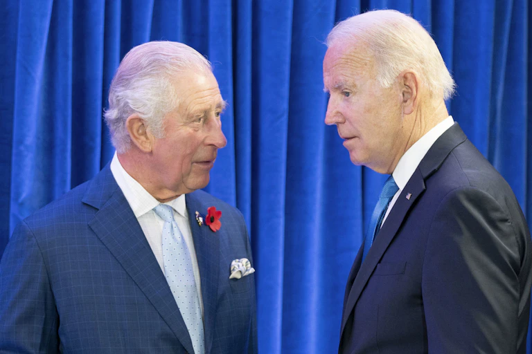 Two men wearing blue suits chat.