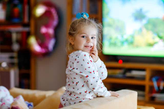 Young child stands on sofa in front of TV screen