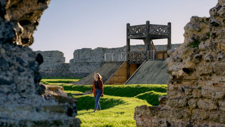 A woman walking by the gateway and ruined walls in the sun.
