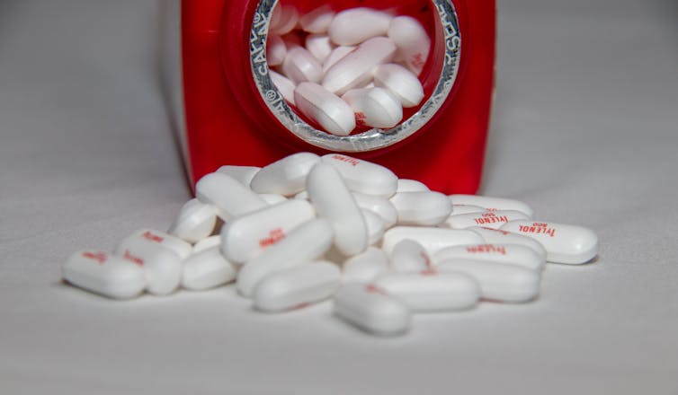 A open bottle of acetaminophen lying on its side with caplets spilling out