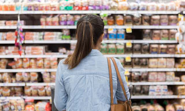 Woman with a pony tail carrying a purse stares at shelves of bread.