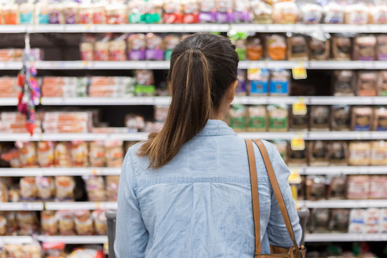 Woman with a pony tail carrying a purse stares at shelves of bread.