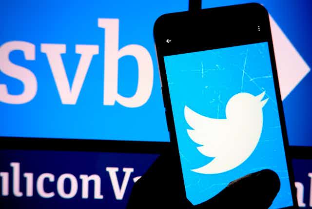 Twitter logo on a phone against an illuminated SVB logo in the bakground.
