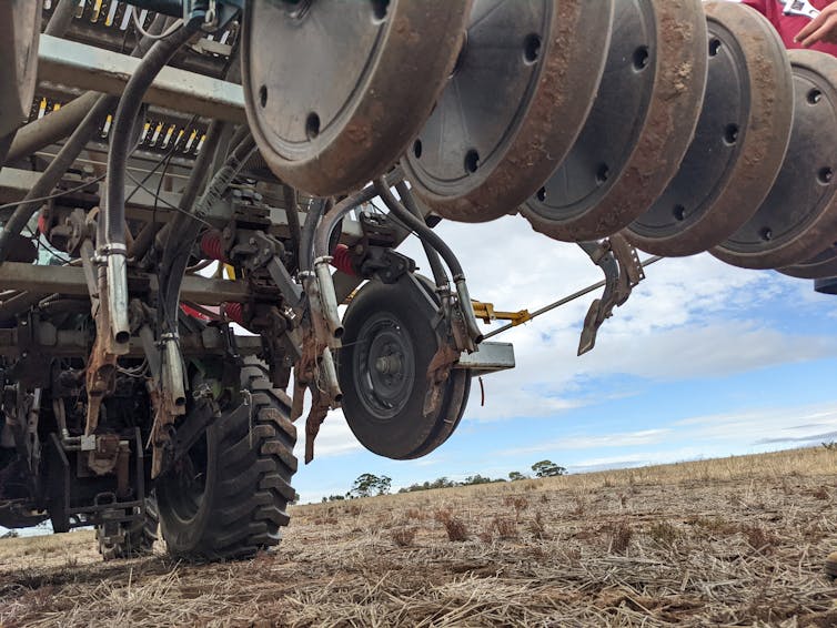 Close-up of a tractor with equipment attached that features rows of digging and seed-depositing tools