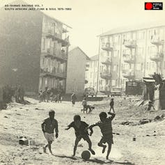 An album cover featuring a sepia toned photo of young boys playing soccer in a street with high-rise housing and shacks.