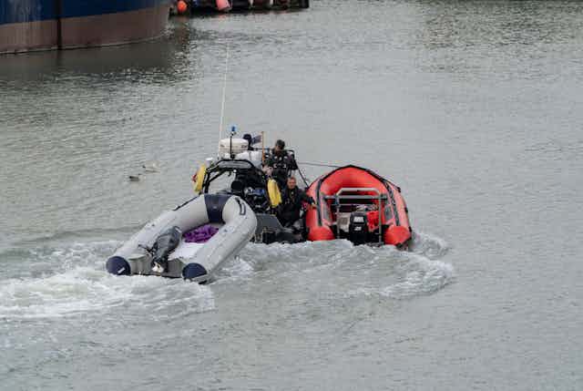 A Border Force boat pulls along two small, empty inflatable boats into a Dover port