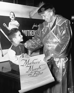 Eleanor Roosevelt smiles with a young boy holding a 'Mothers March on Polio' scroll