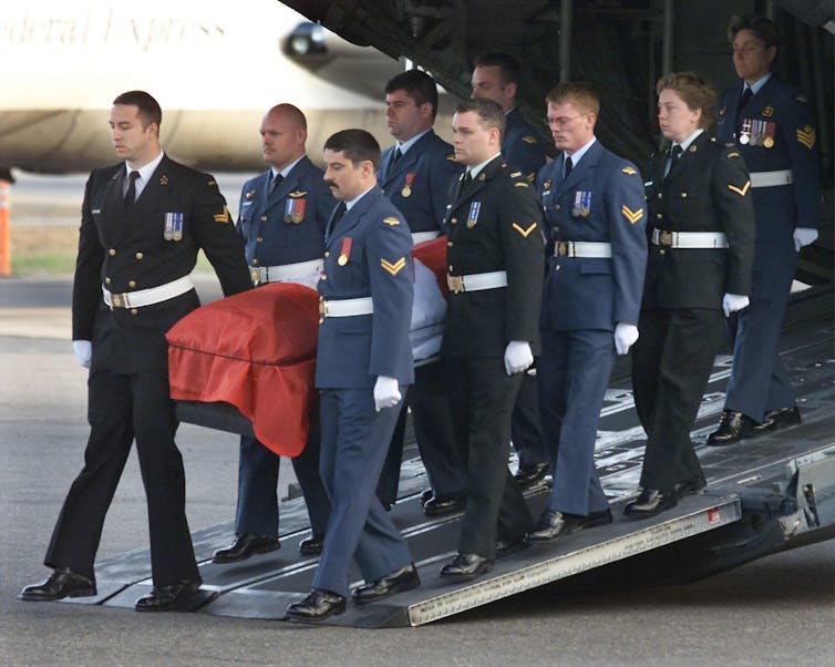 Pallbearers carry the flag-draped casket of a soldier from a Hercules transport aircraft.