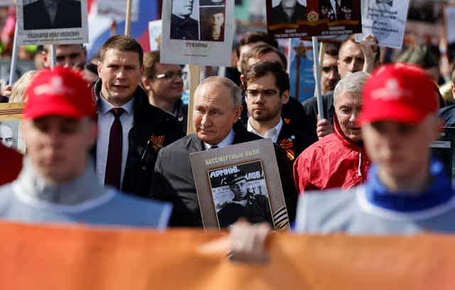 Vladimir Putin among a crowd of people carrying large black and white portrait photos.