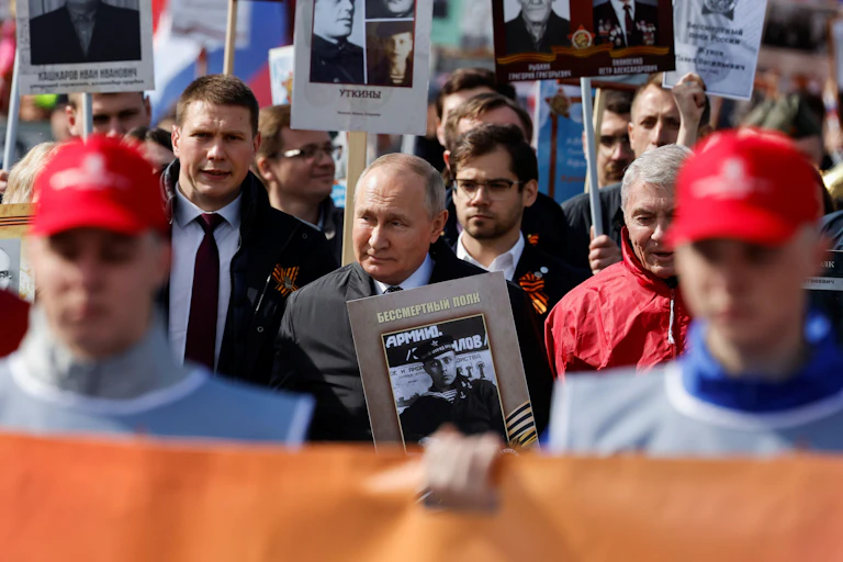 Vladimir Putin among a crowd of people carrying large black and white portrait photos.