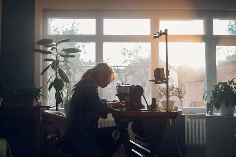 A woman leans over a sewing machine by the window