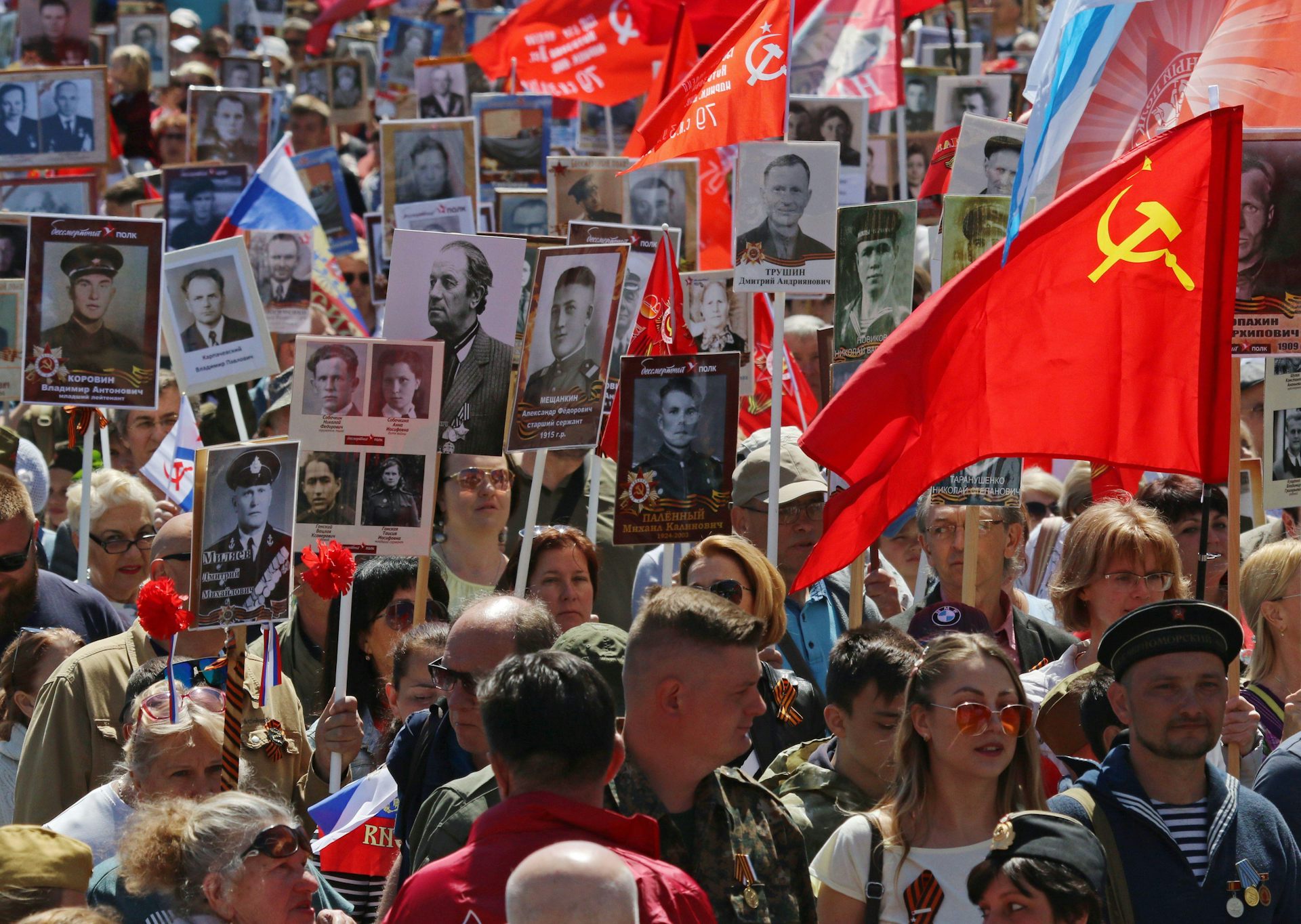 Crowd of people carrying Soviet flags and large black and white portrait photos.