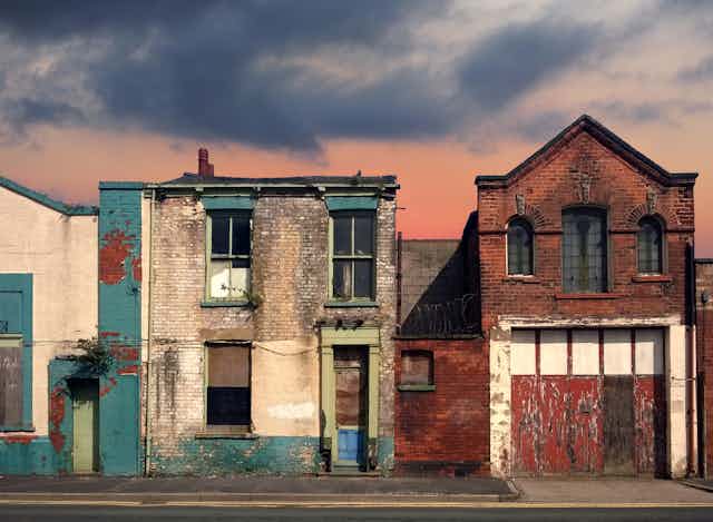 a deserted street of old abandoned ruined houses with bright peeling paint and crumbling brickwork in evening sunlight against a bright cloudy sunset sky