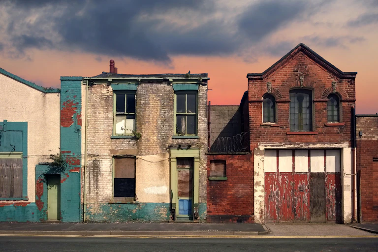 a deserted street of old abandoned ruined houses with bright peeling paint and crumbling brickwork in evening sunlight against a bright cloudy sunset sky