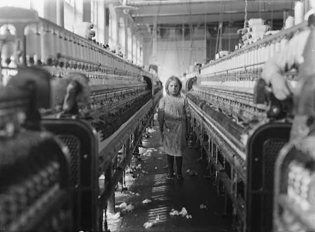 A girl looking at the camera in the middle of a textile factory.