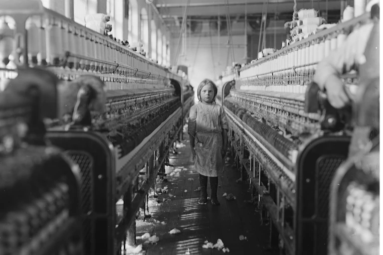 A girl looking at the camera in the middle of a textile factory.