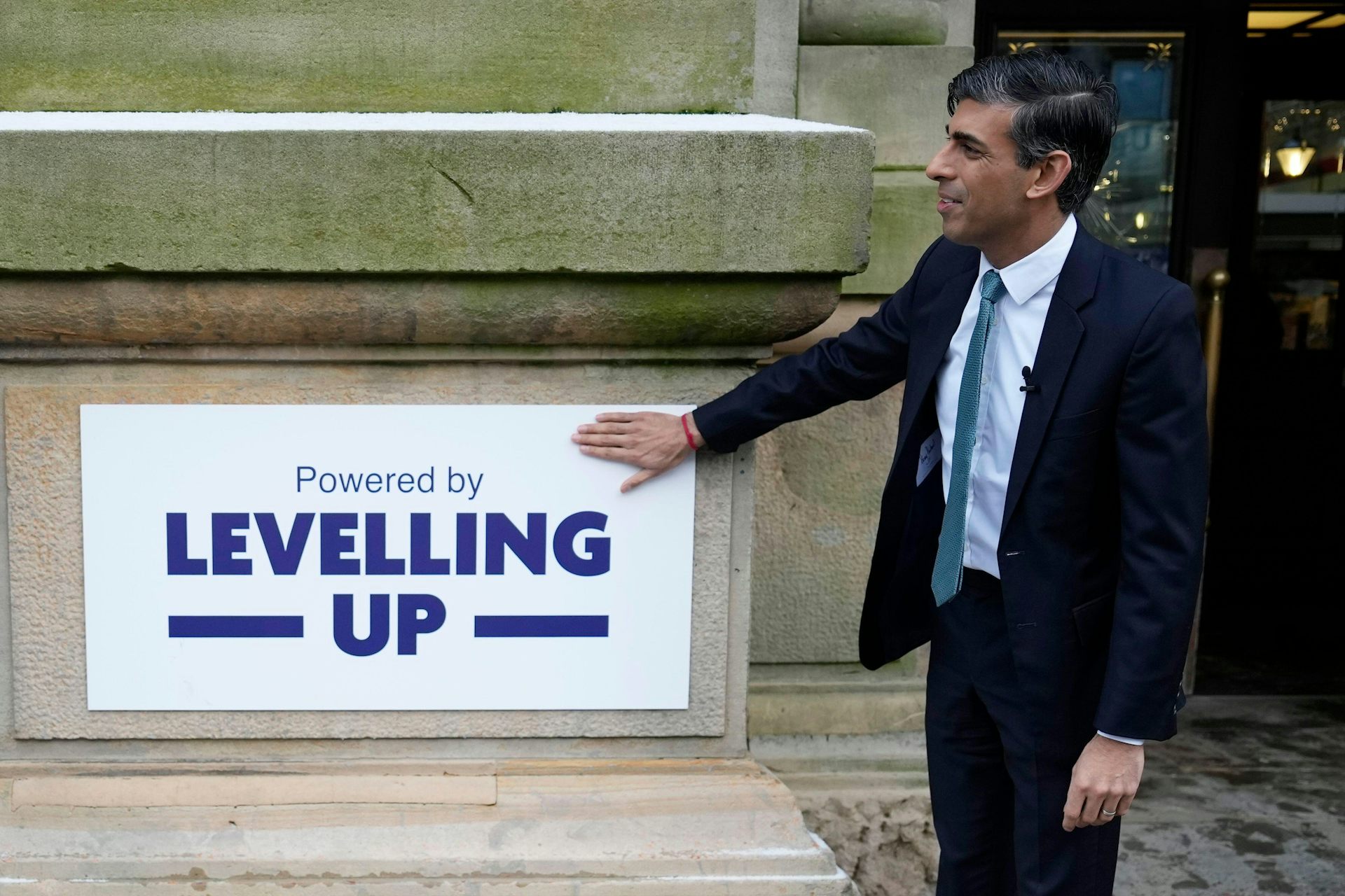 UK PM Rishi Sunak stands in front of a sign that says 