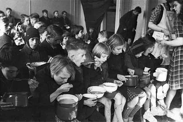 Children eat from pots sitting in rows.