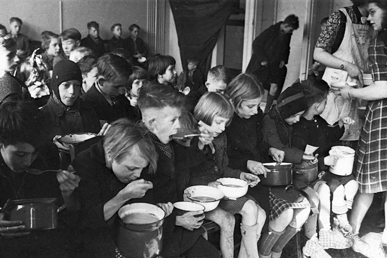 Children eat from pots sitting in rows.