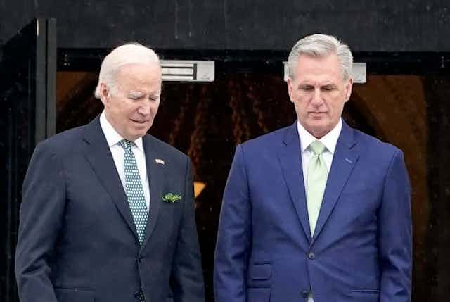 Two white men with gray hair wearing suits walk down steps next to each other facing forward