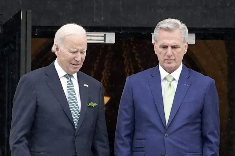 Two white men with gray hair wearing suits walk down steps next to each other facing forward