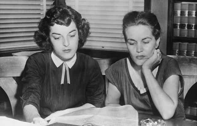 Two young women sit next to each other and look down in a black and white photo. 