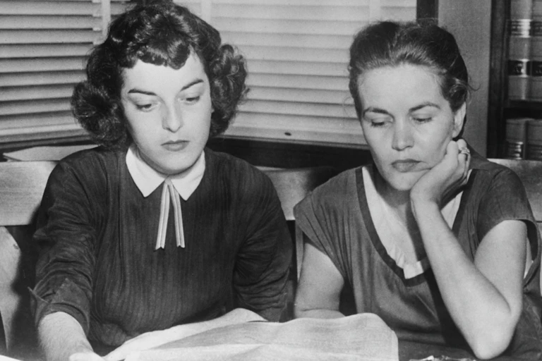 Two young women sit next to each other and look down in a black and white photo.