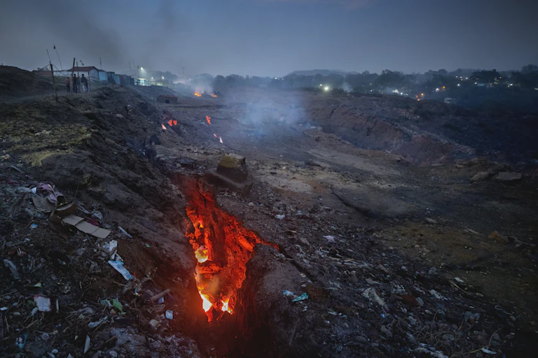 Large cracks in surface rock expose a red glow from fires below.