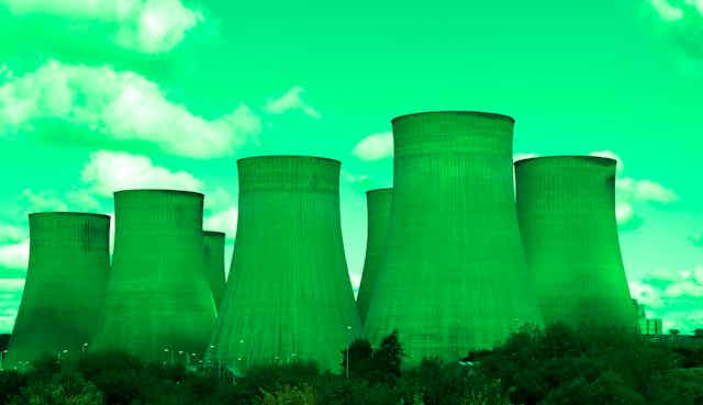Against a computer-generated green sky, seven green smokestacks sit in an industrial area.