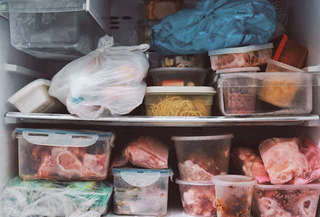 A messy freezer full of food containers including raw meat and pasta, and plastic bags