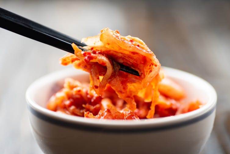 Close-up of chopsticks picking up a piece of kimchi from a white bowl