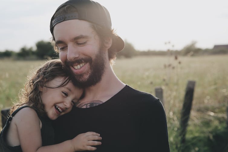 man is carrying small child and both look happy near grassy field