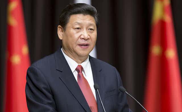 President Xi in red tie standing in front of flags.