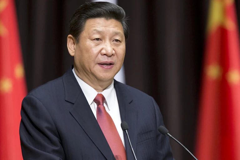 President Xi in red tie standing in front of flags.