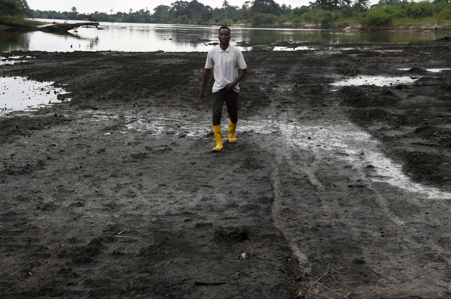 Man on the shore of a river polluted by crude oil