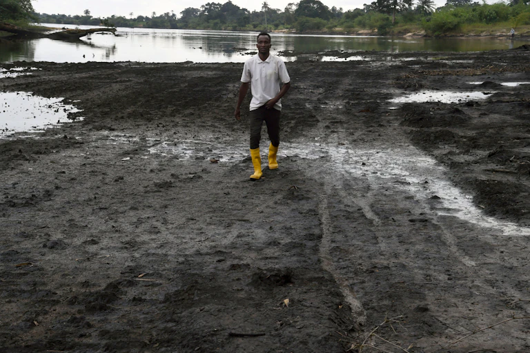 Man on the shore of a river polluted by crude oil