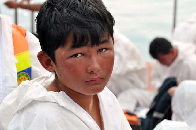 An Indonesian boy looks at the camera, sadly, wearing a rain slicker on a boat