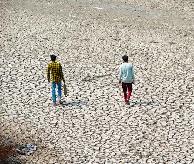 Two people walk along a dried up river bed.