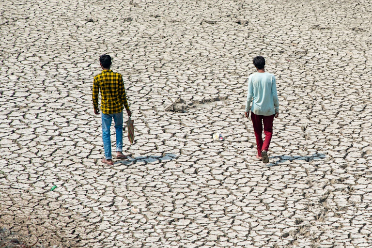 Two people walk along a dried up river bed.