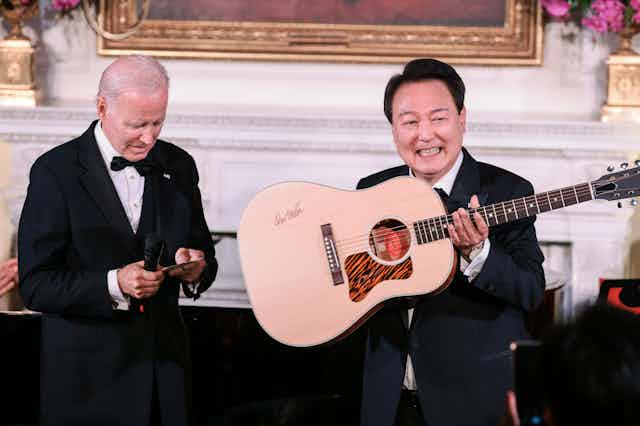 US president Joe Biden looks on as SOuth Korean president Yoon Suk-yeol holds up a guitar