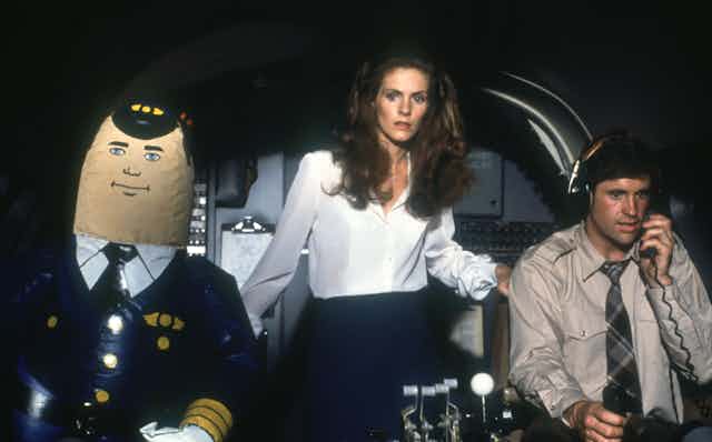 A blow-up autopilot, a sweating man and a woman looking scared are in an airplane cockpit!