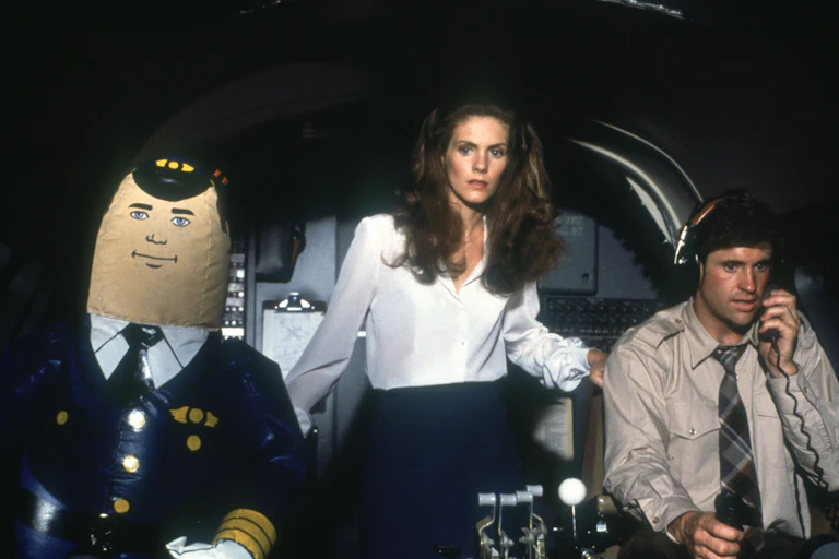 A blow-up autopilot, a sweating man and a woman looking scared are in an airplane cockpit!