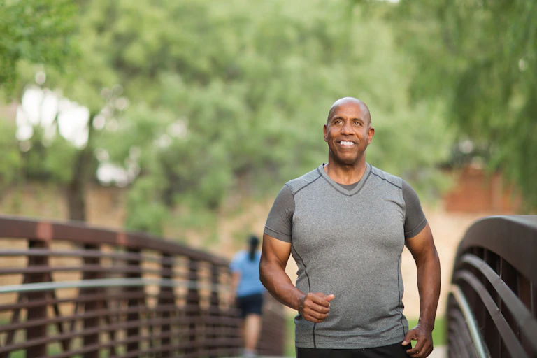Man in a gray t-shirt crossing a foorbridge in a park