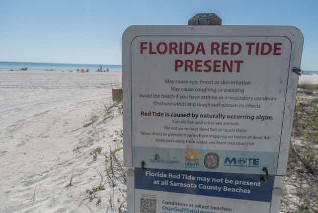 A sign at the entrance to an empty beach warns of red tide. 