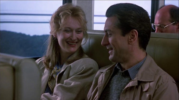 Una mujer y un hombre viajan en tren y se ríen.