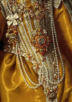 Detalle de la ropa de una mujer del siglo de oro con grandes joyas y cadenas.